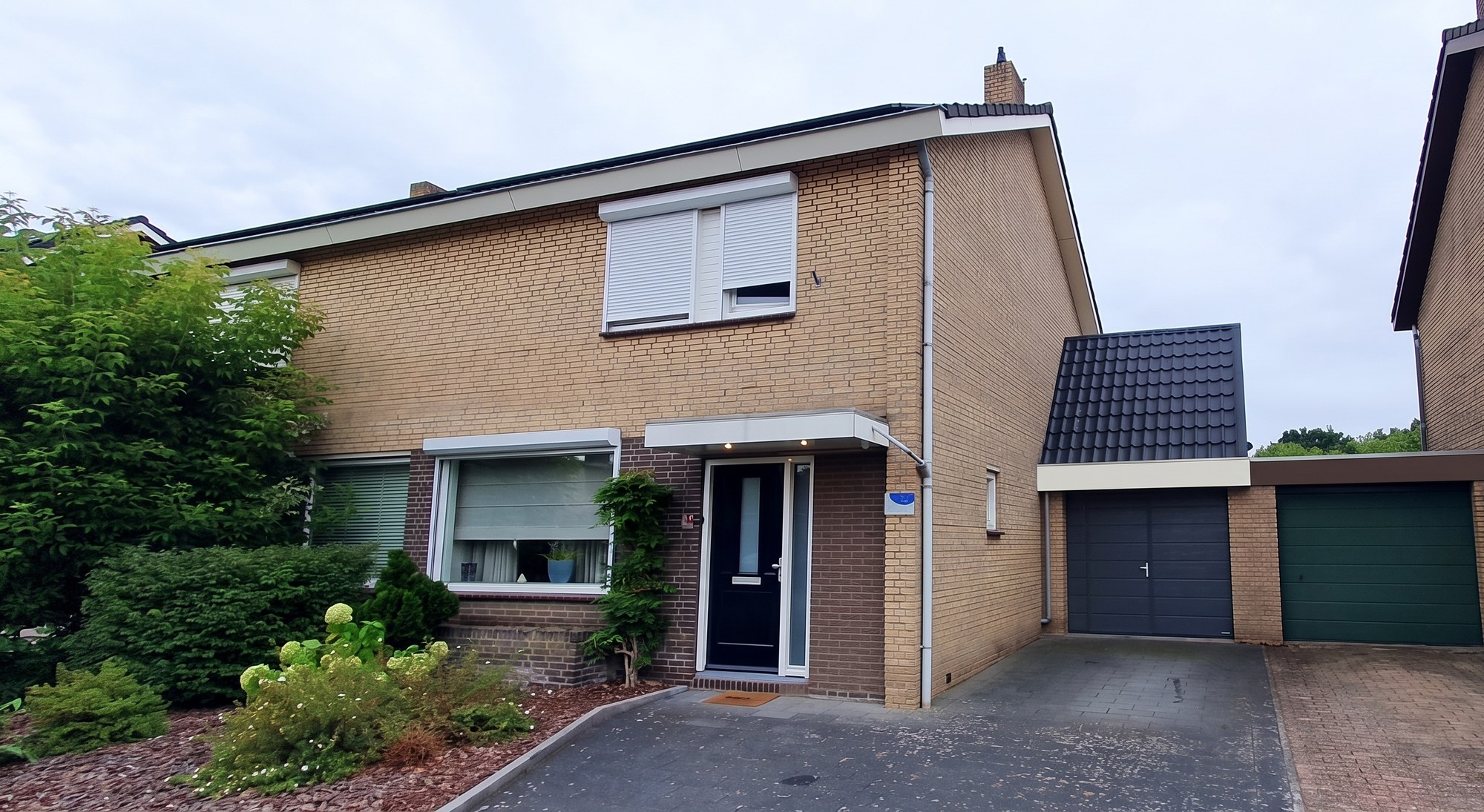 De garage vanaf de straat, met de nieuwe kap boven de bestaande garagedeur en het boeiboord dat in dezelfde maat doorloopt naar de garage van de buren