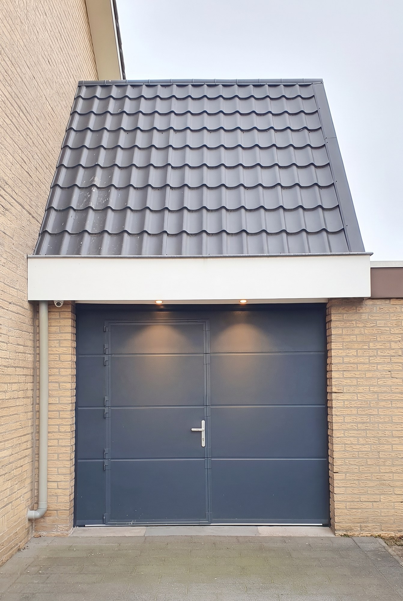 De opgetopte garage frontaal vanaf de oprit, met het witte boeiboord tussen de bestaande garagedeur en de nieuwe kap
